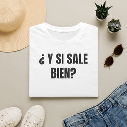 Camiseta blanca ¿Y SI SALE BIEN? doblada junto a unos vaqueros, gafas de sol y un sombrero de paja