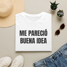 Camiseta blanca ME PARECIÓ BUENA IDEA doblada junto a unos vaqueros, gafas de sol y un sombrero de paja