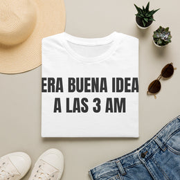 Camiseta blanca ERA BUENA IDEA A LAS 3 AM doblada junto a unos vaqueros, gafas de sol y un sombrero de paja